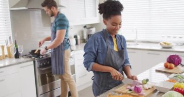 Video of happy diverse couple preparing meal, cutting vegetables in kitchen. Love, relationship and spending quality time together at home.