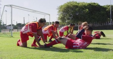 Video of diverse group of male football players warming up on field,doing sit -ups. Male football team, inclusivity and fitness in team sports.