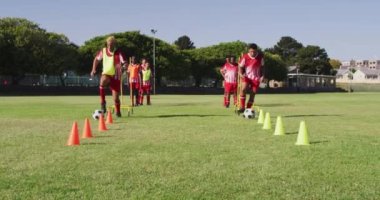 Video of diverse group of male football players warming up on field,running and kicking ball. Male football team, inclusivity and fitness in team sports.