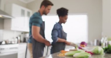 Video of happy diverse couple preparing meal, cutting vegetables in kitchen. Love, relationship and spending quality time together at home.