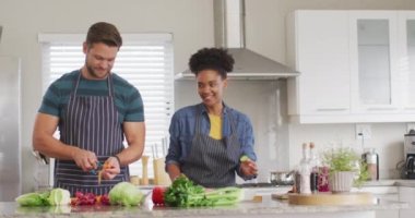 Video of happy diverse couple preparing meal, cutting vegetables in kitchen. Love, relationship and spending quality time together at home.