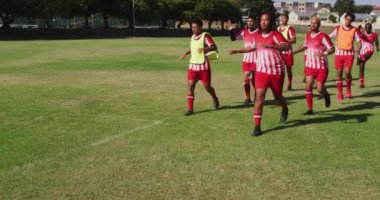 Video of diverse group of male football players warming up on field, running. Male football team, inclusivity and fitness in team sports.