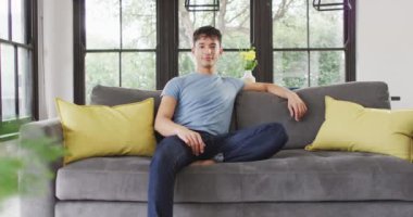 Portrait of happy biracial man sitting on sofa, looking at camera and smiling. Spending quality time at home.