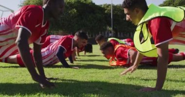Video of diverse group of male football players warming up on field,doing push-ups. Male football team, inclusivity and fitness in team sports.