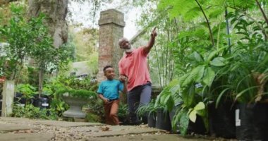 Mutlu kıdemli Afro-Amerikan adam ve torunu bahçede dolaşıp bitkilere bakıyor. Dışarıda vakit geçirmek, bahçede çalışmak..