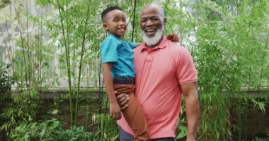 Torunuyla bahçede kucaklaşan mutlu bir Afrikalı Amerikalı adamın portresi. Dışarıda vakit geçirmek, bahçede çalışmak..