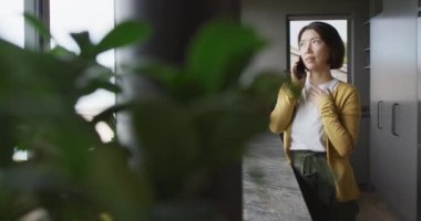 Asyalı kadın kazak giyiyor ve mutfakta tek başına akıllı telefonla konuşuyor. Evde kaliteli zaman geçirmek.