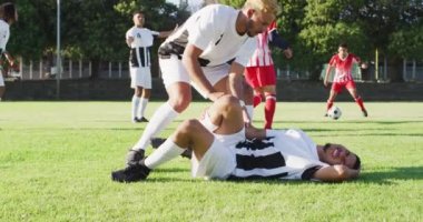 Video of the biracial player helps the fouled teammate on field. Male football team, inclusivity and fitness in team sports.