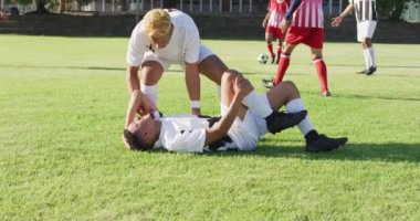 Video of two diverse footballers helping fouled teammate. Male football team, inclusivity and fitness in team sports.
