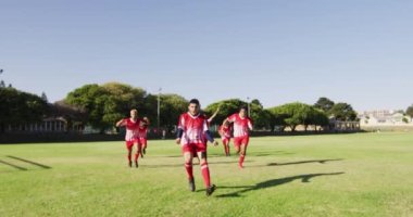 Video of happy diverse group of football players running on field with ball. Male football team, inclusivity and fitness in team sports.