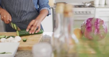 Video of midsection of caucasian man cutting cucumber in kitchen. Lifestyle, cooking, household and spending time at home concept.