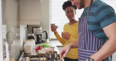 Video of happy diverse couple preparing meal in kitchen. Love, relationship and spending quality time together at home.