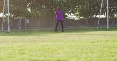 Video of african american goalkeeper on field, playing football. Male football team, inclusivity and fitness in team sports.