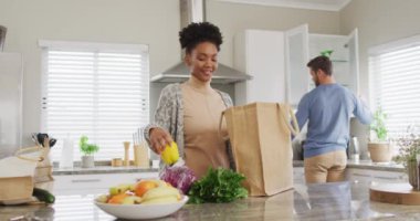Video of african american woman unpacking groceries in kitchen. Love, relationship and spending quality time together at home.