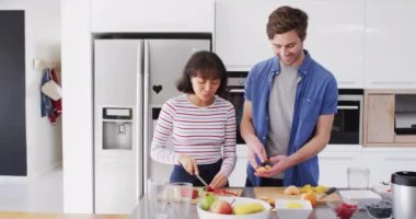 Video of happy diverse couple preparing meal together in kitchen. Love, relationship and spending quality time together concept.