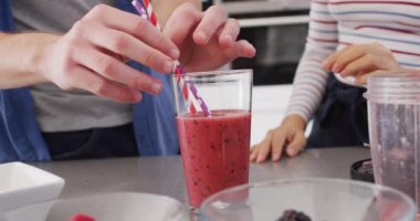 Video of midsection of diverse couple putting straws into glass with juice. Love, relationship and spending quality time together concept.