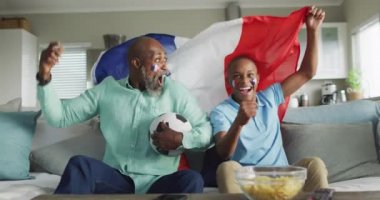 Afrika kökenli Amerikalı baba ve oğlunun Fransa bayrağı taşıyan TV 'deki maçı videosu. Aile zamanı, ev kavramında birlikte zaman geçirmek..