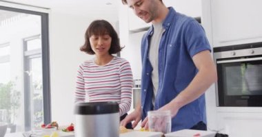Video of happy diverse couple preparing meal together in kitchen. Love, relationship and spending quality time together concept.