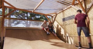 Video of happy diverse female and male skateboarders training in skate park. Skateboarding, sport, hobby and active lifestyle concept.