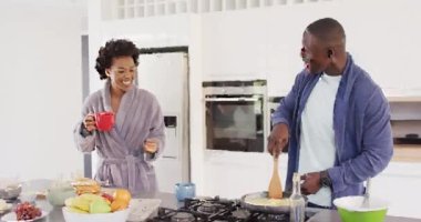 Video of happy african american couple preparing breakfast and coffee together in kitchen. Love, relationship and spending quality time together concept.