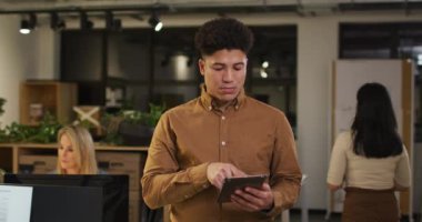 Elinde tabletle geç saatlere kadar çalışan çift ırklı bir adamın videosu. İş ve ofiste geceleri teknoloji konseptiyle çalışmak.
