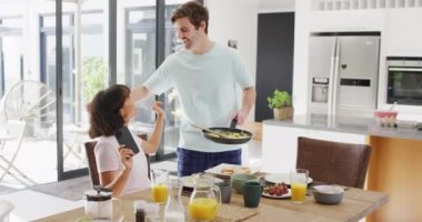 Video of happy diverse couple eating breakfast together in kitchen. Love, relationship and spending quality time together concept.