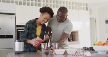 Video of happy african american couple preparing juice together in kitchen. Love, relationship and spending quality time together concept.