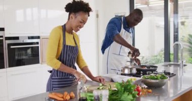 Video of happy african american couple preparing meal together in kitchen. Love, relationship and spending quality time together concept.