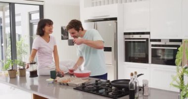 Video of happy diverse couple drinking coffee together in kitchen. Love, relationship and spending quality time together concept.