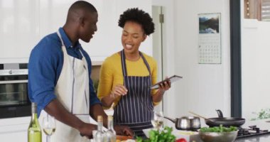 Video of happy african american couple cooking together with tablet. Love, relationship and spending quality time together concept.
