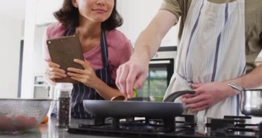 Video of happy diverse couple preparing meal together with tablet. Love, relationship and spending quality time together concept.