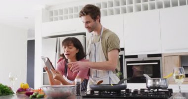 Video of happy diverse couple preparing meal together with tablet. Love, relationship and spending quality time together concept.
