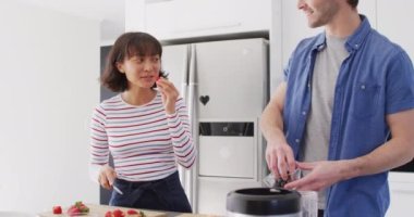 Video of happy diverse couple preparing meal together in kitchen. Love, relationship and spending quality time together concept.