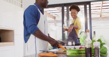 Video of happy african american couple cooking together and drinking wine. Love, relationship and spending quality time together concept.