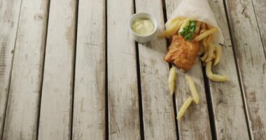 Video of wrapped fish and chips with dip, on rustic table top with copy space. tasty hot homemade fast food meal.