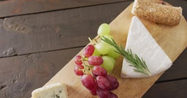 Video of cheeses, grapes, nuts and rosemary on chopping board, on wooden table with copy space. quality, tasty light food snack.