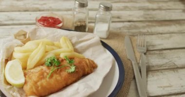 Video of fish and chips on plate, salt and pepper and ketchup on wooden table. tasty hot fast food meal.