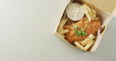 Video of fish and chips with dip in takeaway food box, with copy space on white background. tasty hot fast food meal.