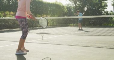 Video of happy biracial couple playing tennis on the court. Healthy active lifestyle and fitness at home.