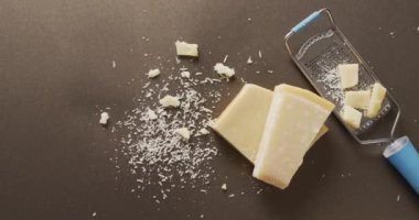 Video of block of parmesan cheese and cheese grater cheese on wooden table. savoury cooking ingredient and food preparation.