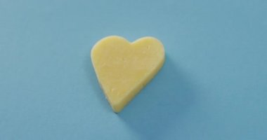 Video of heart shape of cheese on blue background with copy space. savoury food, fun cheese lovers snack.