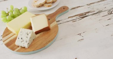 Video of cheeses on chopping board, with grapes and bread on rustic wooden table with copy space. quality, tasty light food snack.
