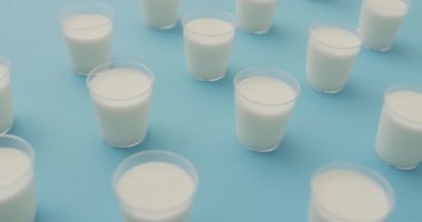 Video of row of glasses of milk on blue background. dairy products and healthy organic nutrition.
