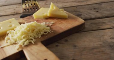 Video of yellow cheese and grated cheese on wooden board with cheese grater on rustic table. savoury cooking ingredient and food preparation.