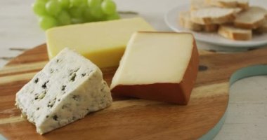 Video of assorted cheeses on chopping board, with grapes and bread on rustic wooden table. quality, tasty light food snack.