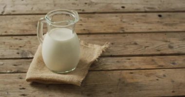 Video of glass jug of milk on wooden background. dairy products and healthy organic nutrition.