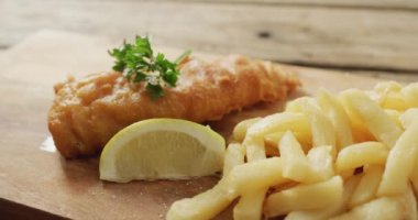 Video of fish and chips with lemon wedge on wooden board, on rustic table. tasty hot homemade fast food meal.