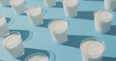 Video of row of glasses of milk on blue background. dairy products and healthy organic nutrition.