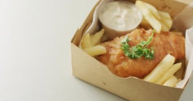 Video of fish and chips with dip in takeaway food box, with copy space on white background. tasty hot fast food meal.