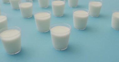 Video of row of glasses of milk on blue background. dairy products and healthy organic nutrition.